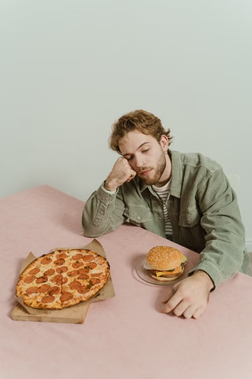 Hombre con pizza y hamburguesa, cansado de comer mal